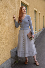 Load image into Gallery viewer, Woman in a light blue cardigan and plaid skirt standing against a beige wall.