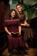 Load image into Gallery viewer, Two women posing in matching vintage-style brown and burgundy dresses with geometric patterns, set in a dimly lit indoor environment with wooden furniture and a potted plant.