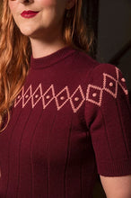 Load image into Gallery viewer, A close-up of a woman wearing a short-sleeve ribbed knit sweater in deep burgundy with a contrasting light pink geometric diamond pattern across the chest and shoulders.