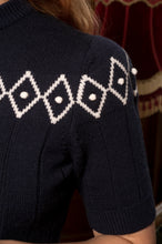 Load image into Gallery viewer, Close-up of a navy blue short-sleeve knit sweater with a white diamond argyle pattern across the chest and shoulder, worn by a model.