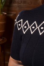 Load image into Gallery viewer, Close-up of a navy blue knit sweater with a white geometric diamond pattern across the upper chest, worn by a person in a warm indoor setting.