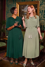 Load image into Gallery viewer, Two women standing indoors wearing elegant midi dresses, one in emerald green and the other in sage green, holding cocktail glasses in a decorated room with patterned wallpaper and a large framed painting.