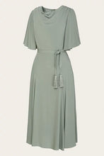 Load image into Gallery viewer, A sage green midi dress with a draped cowl neckline, short flutter sleeves, a matching waist tie with tassel details, and a flared skirt, shown against a plain light beige background.