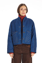 Load image into Gallery viewer, A model wearing a cropped blue denim jacket with diagonal contrast stitching, styled over a red turtleneck and brown pants, against a plain white background.