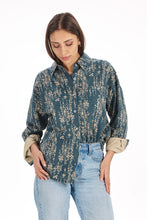 Load image into Gallery viewer, A woman wearing a dark teal-green button-up shirt with a beige floral pattern and rolled-up sleeves, paired with light-wash blue jeans, against a plain white background.