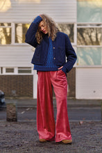Load image into Gallery viewer, A woman stands outdoors in front of a building, wearing a navy quilted jacket over a blue patterned sweater, paired with bright pink wide-leg velvet pants and tan boots.