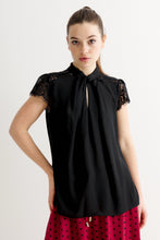 Load image into Gallery viewer, A woman modeling a black short-sleeve blouse with lace cap sleeves and a front tie-neck detail, paired with a red polka-dot skirt, against a plain light gray studio background.