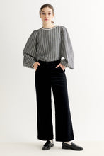 Load image into Gallery viewer, A woman modeling a black and white vertically striped long-sleeve blouse with a beaded collar and black wide-leg courderoy trousers, standing against a plain white studio background.
