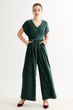 Load image into Gallery viewer, A woman modeling a dark green velvet wide-leg jumpsuit with a tie waist and short sleeves, paired with burgundy heels, against a plain white studio background.