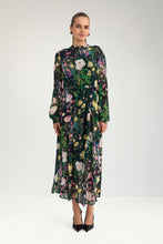 Load image into Gallery viewer, A woman modeling a long-sleeved midi dress with a dark green base and a colorful floral print in pink, yellow, white, and purple, paired with black pointed-toe heels against a light gray studio background.