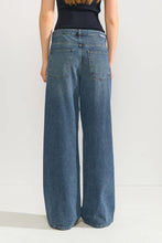 Load image into Gallery viewer, A model shown from the back wearing a pair of wide-leg blue denim jeans with a dark ribbed top, set against a plain light gray studio background.