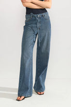 Load image into Gallery viewer, A person wearing wide-leg blue denim jeans with a drawstring waist, paired with a black ribbed top and dark sandals, photographed against a light gray studio background.