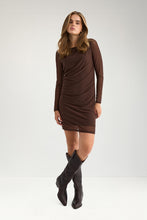 Load image into Gallery viewer, A woman modeling a fitted, long-sleeve brown mini dress with ruched draping details, paired with black knee-high boots, against a plain light gray studio background.