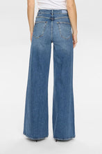 Load image into Gallery viewer, A person shown from the back wearing blue wide-leg denim jeans with a white top, photographed against a light gray studio background.