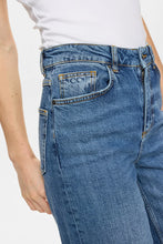 Load image into Gallery viewer, Close-up of a person wearing medium-wash blue denim jeans with a white top, showing the back pocket and waistband area against a plain light background.
