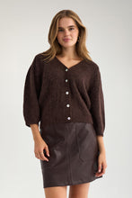 Load image into Gallery viewer, A woman modeling a dark brown fuzzy button-front cardigan with three-quarter sleeves, paired with a dark brown faux-leather mini skirt, against a plain light gray studio background.