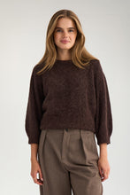 Load image into Gallery viewer, A woman modeling a dark brown fuzzy knit sweater with three-quarter sleeves, paired with brown trousers, against a plain light gray studio background.