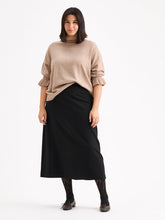 Load image into Gallery viewer, A woman modeling a beige long-sleeve knit sweater with ruffled cuffs and a black midi skirt, paired with black lace-up shoes and patterned tights, against a plain white studio background.