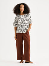 Load image into Gallery viewer, Woman wearing a patterned top and brown pants on a white background