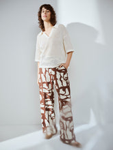 Load image into Gallery viewer, Woman wearing a white textured top and patterned brown pants against a plain background