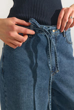 Load image into Gallery viewer, Close-up of a person wearing blue denim jeans with a dark ribbed top, showing hands adjusting the waistband and belt loops.