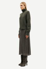 Load image into Gallery viewer, A model is shown in profile wearing a dark olive green knit turtleneck sweater, a matching dark gray pleated midi skirt, and dark leather heeled boots against a plain light gray background.
