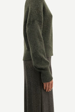 Load image into Gallery viewer, Side view of a person wearing a fuzzy olive green sweater and a dark patterned skirt against a plain light background.