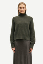 Load image into Gallery viewer, A model wearing a dark olive green knit mock neck sweater and a dark gray textured skirt, photographed against a solid light gray background.