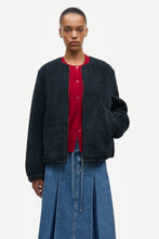Load image into Gallery viewer, A model wearing a dark navy bouclé cropped cardigan over a red button-up shirt and a blue denim skirt, photographed against a solid off-white background.
