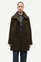 Load image into Gallery viewer, A model wearing a dark olive-brown wool coat over a denim shirt and jeans, photographed against a plain light gray studio background.