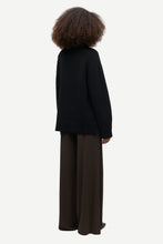 Load image into Gallery viewer, A child model shown from the back wearing a black knit cardigan and dark brown wide-leg trousers, photographed against a solid light gray background.