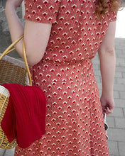 Load image into Gallery viewer, Person wearing a red patterned dress holding a woven basket with a red item inside.
