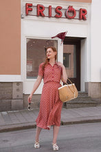 Load image into Gallery viewer, Woman in a red dress standing in front of a building with a sign that reads 'Frisor'.